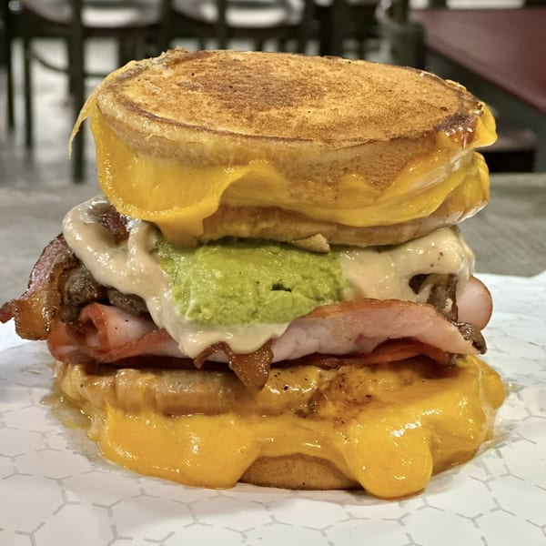 Market Street Burgers' towering burger with melted cheese, bacon, guacamole, and sauce on toasted buns.