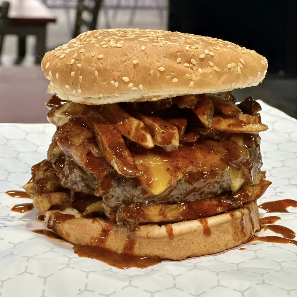 Market Street Burgers' burger with fries, cheese, and sauce overflowing from a sesame seed bun.