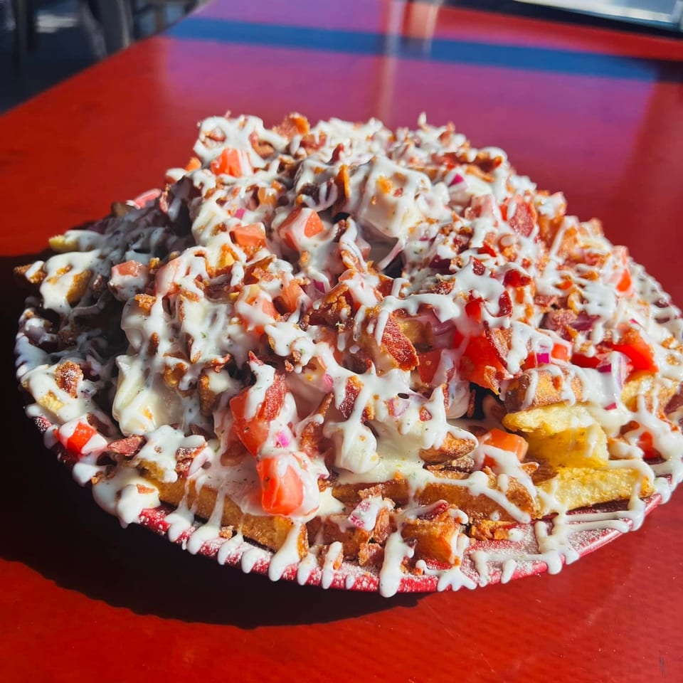 Loaded fries with white sauce, bacon bits, and diced tomatoes on a red plate.