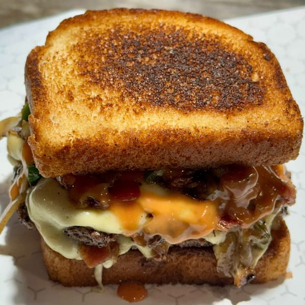 Market Street Burgers' patty melt with melted cheese, bacon, and sauce on toasted bread.