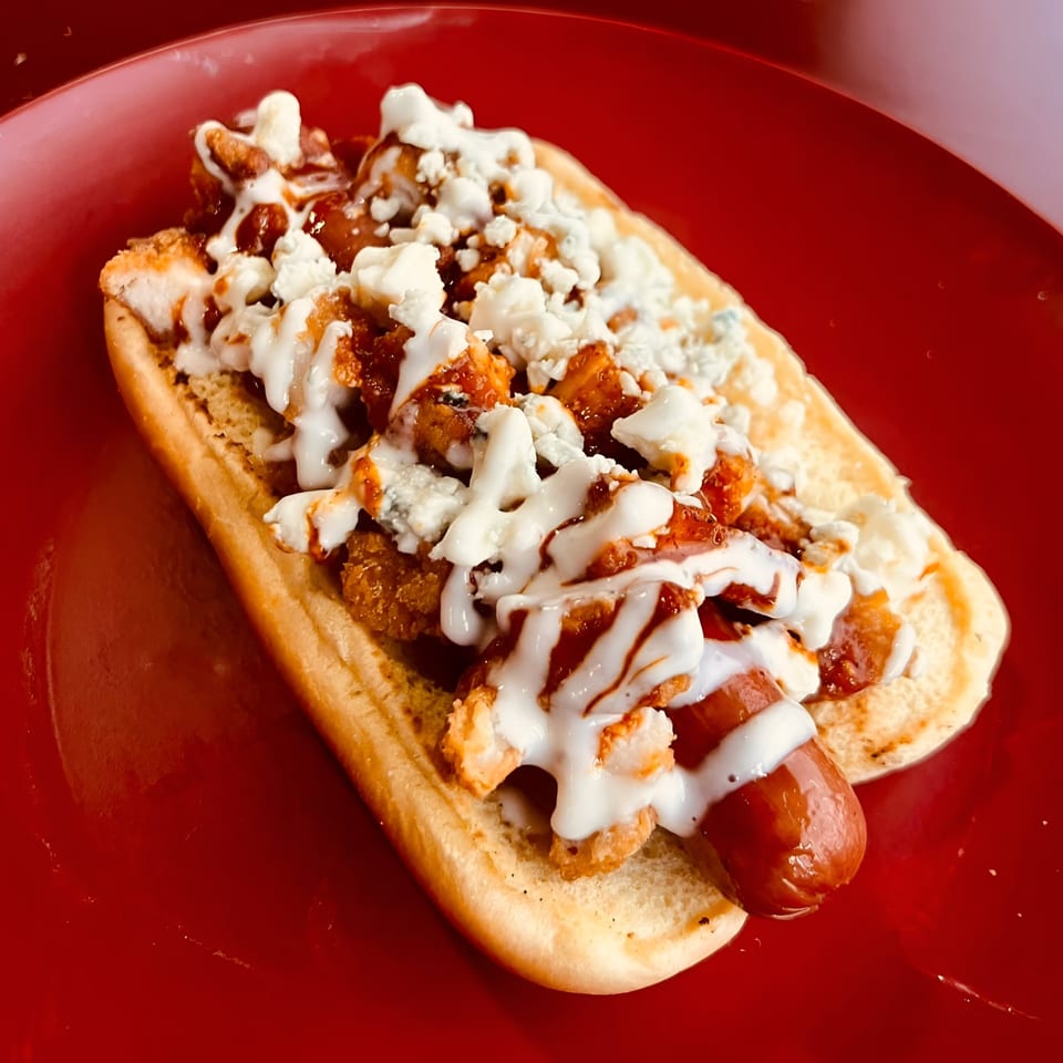 A Market Street Burgers hot dog with crispy chicken, blue cheese, and white sauce on a red plate.