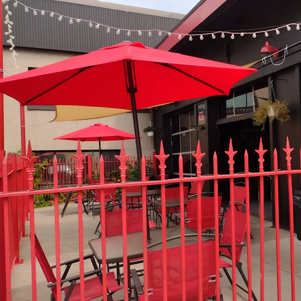 Market Street Burgers' outdoor patio with red umbrellas, tables, chairs, and a red fence.